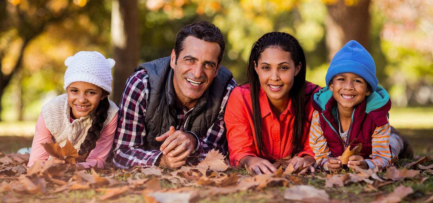 Happy family smiling together outdoors in fall setting at Brooklyn dental practice.