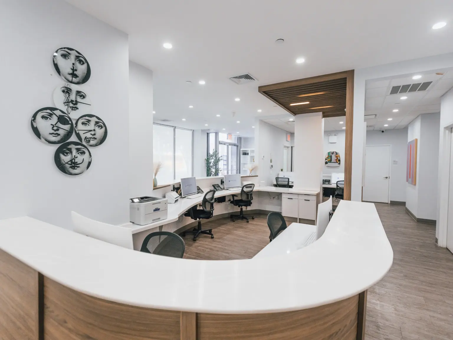 Modern pediatric dental office reception area with curved white desk and artistic face wall decor in Brooklyn.