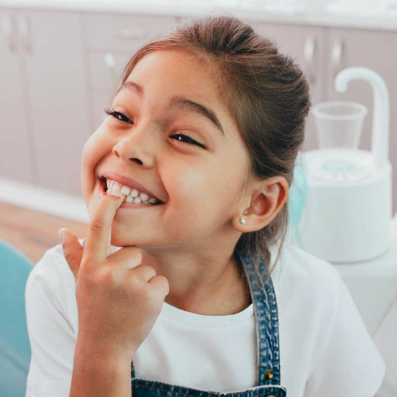 A joyful child points to their healthy smile, representing excellent care from a pediatric dentist in Brooklyn, NY.