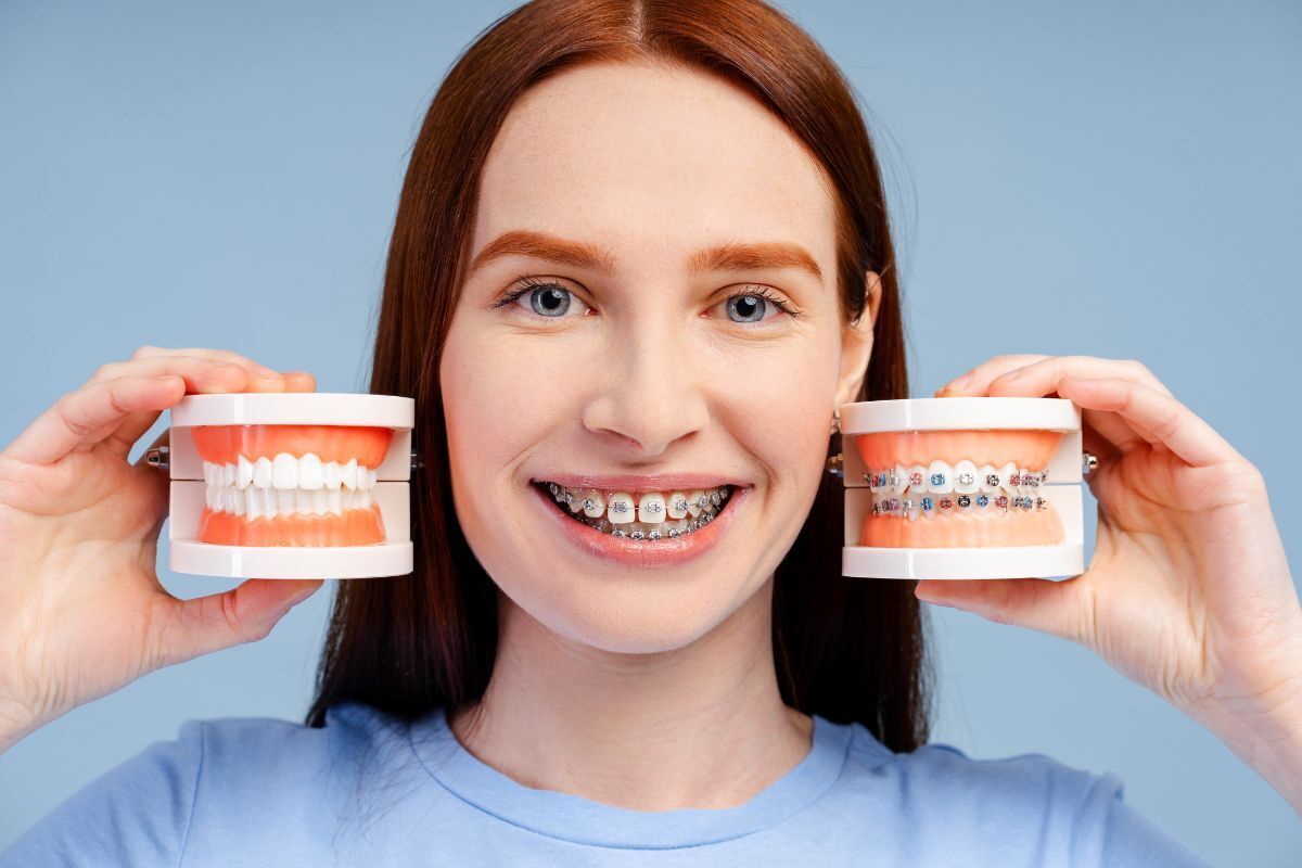 Woman with braces smiling while holding dental models showing orthodontic treatment progression.