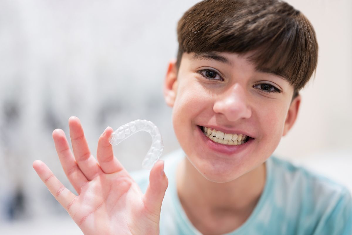 Smiling young boy holding clear orthodontic aligner in Brooklyn dental practice.