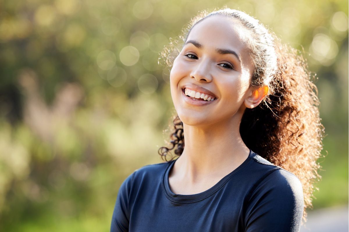 Happy young woman with a bright, confident smile in an outdoor setting.