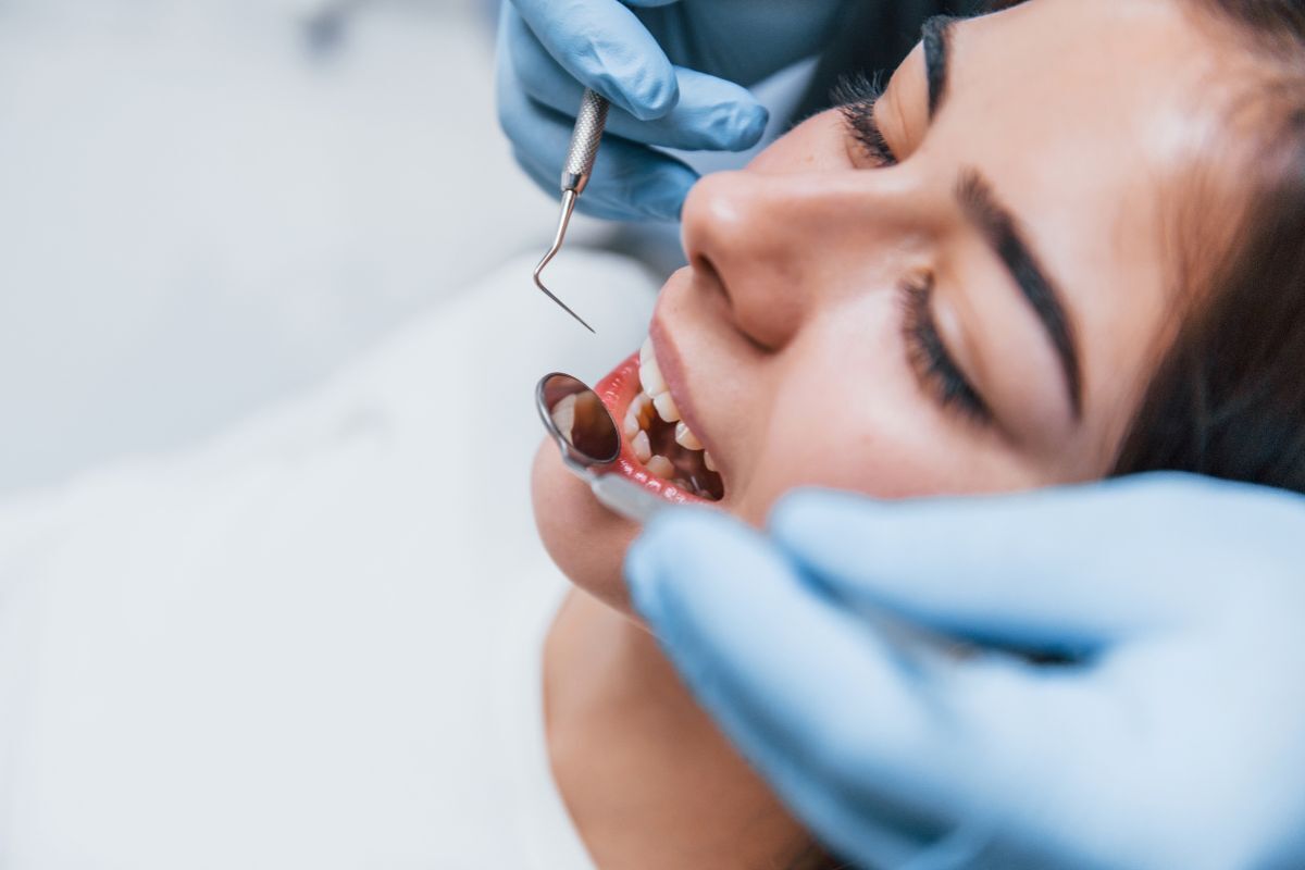 Dentist examining patient's teeth with dental mirror during wisdom tooth extraction consultation in Brooklyn.