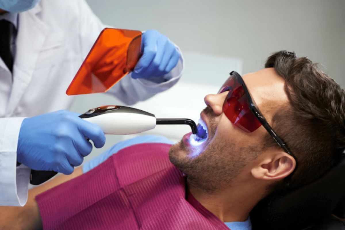 Cosmetic dentist using professional whitening laser treatment on patient's teeth in Brooklyn dental office.