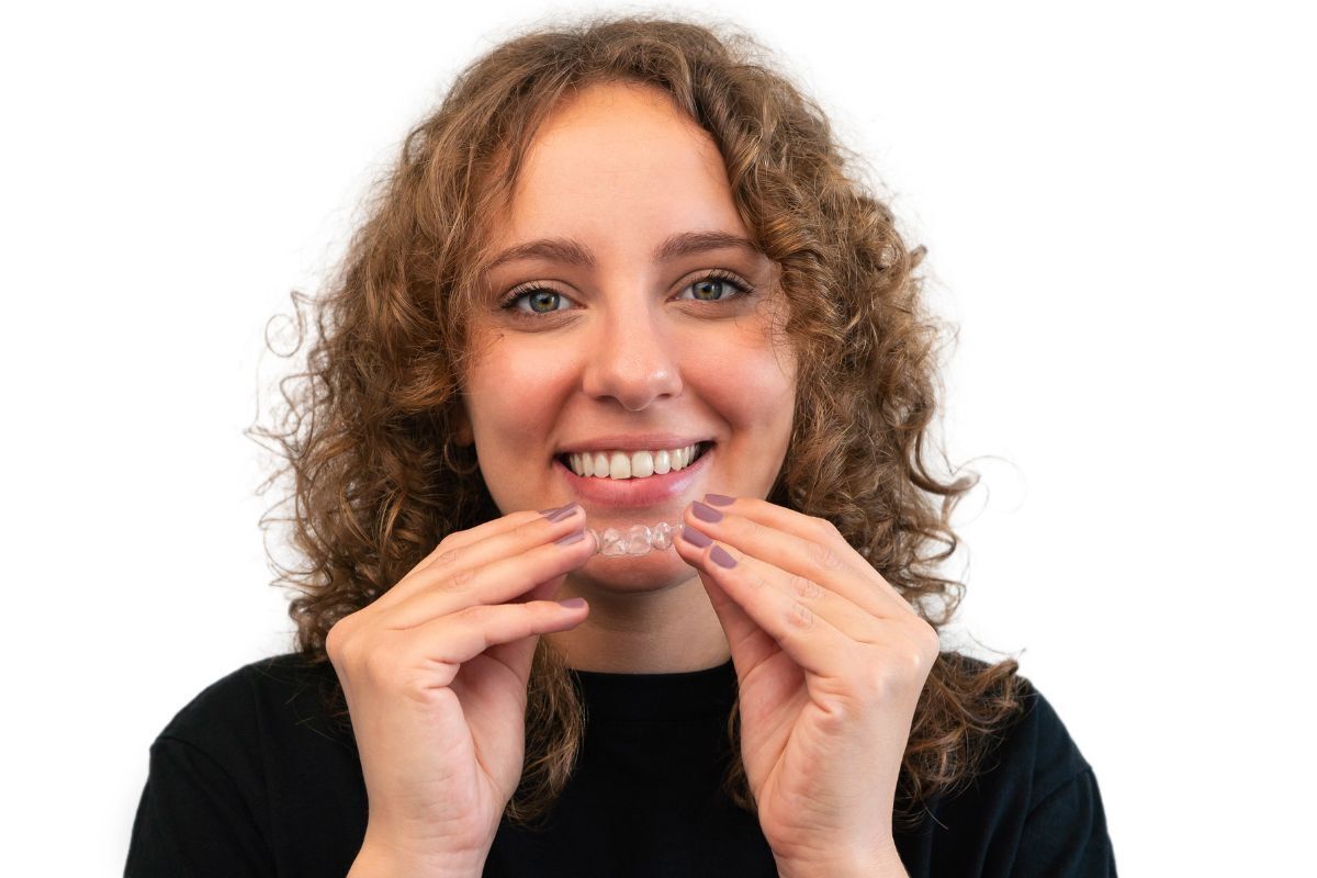 Smiling woman holding clear orthodontic aligner tray for adult braces treatment.