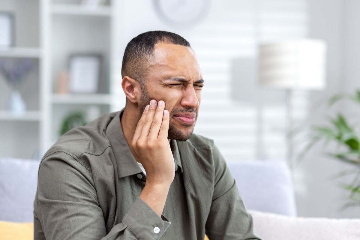 Man holding cheek in pain, representing dental emergency and tooth loss situations requiring urgent care.