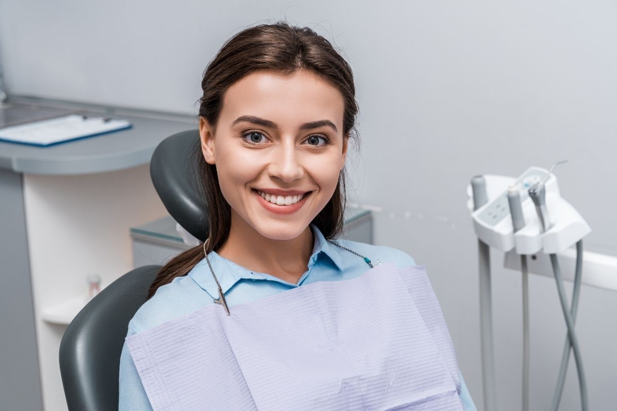 Young woman smiling in dental chair wearing protective bib at Brooklyn dental office.