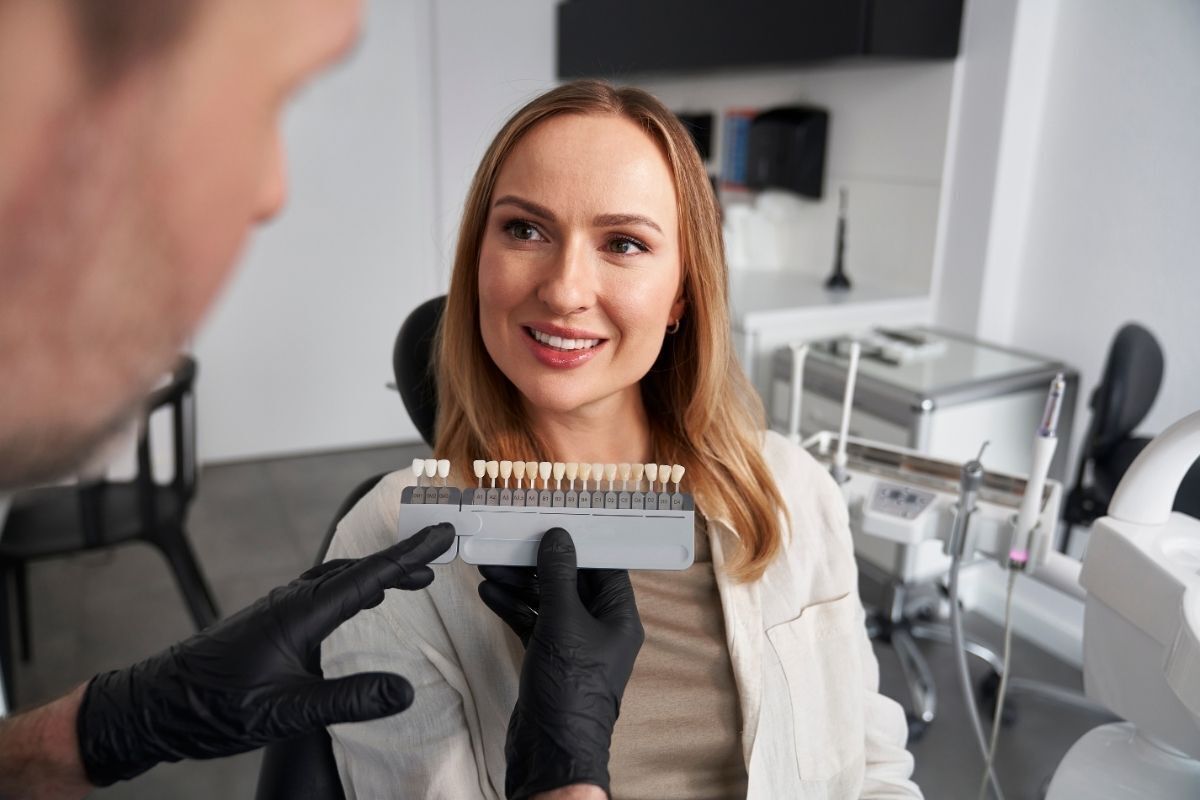 Cosmetic dentist showing shade guide to female patient in Brooklyn dental office.