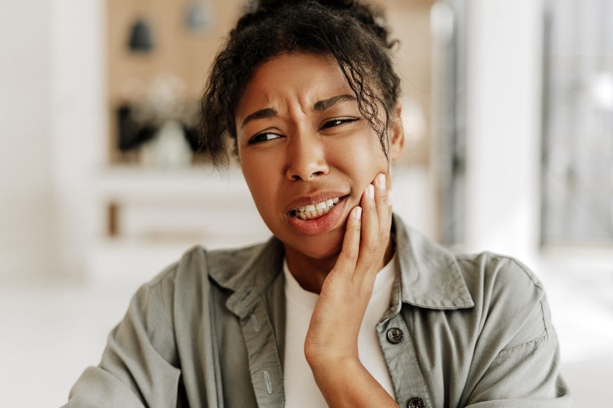 Woman holding her cheek in discomfort, expressing tooth sensitivity pain during dental treatment.