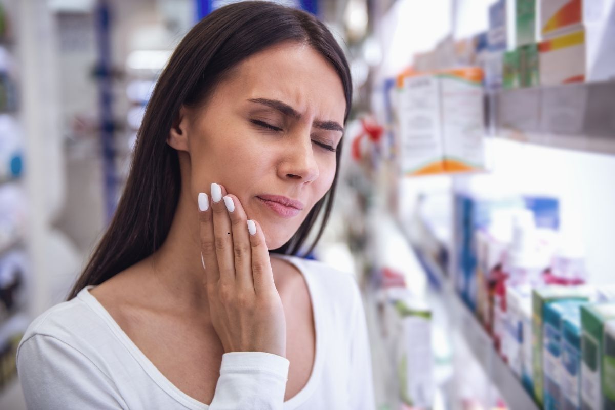 Woman experiencing tooth pain in a pharmacy, seeking emergency dental relief.