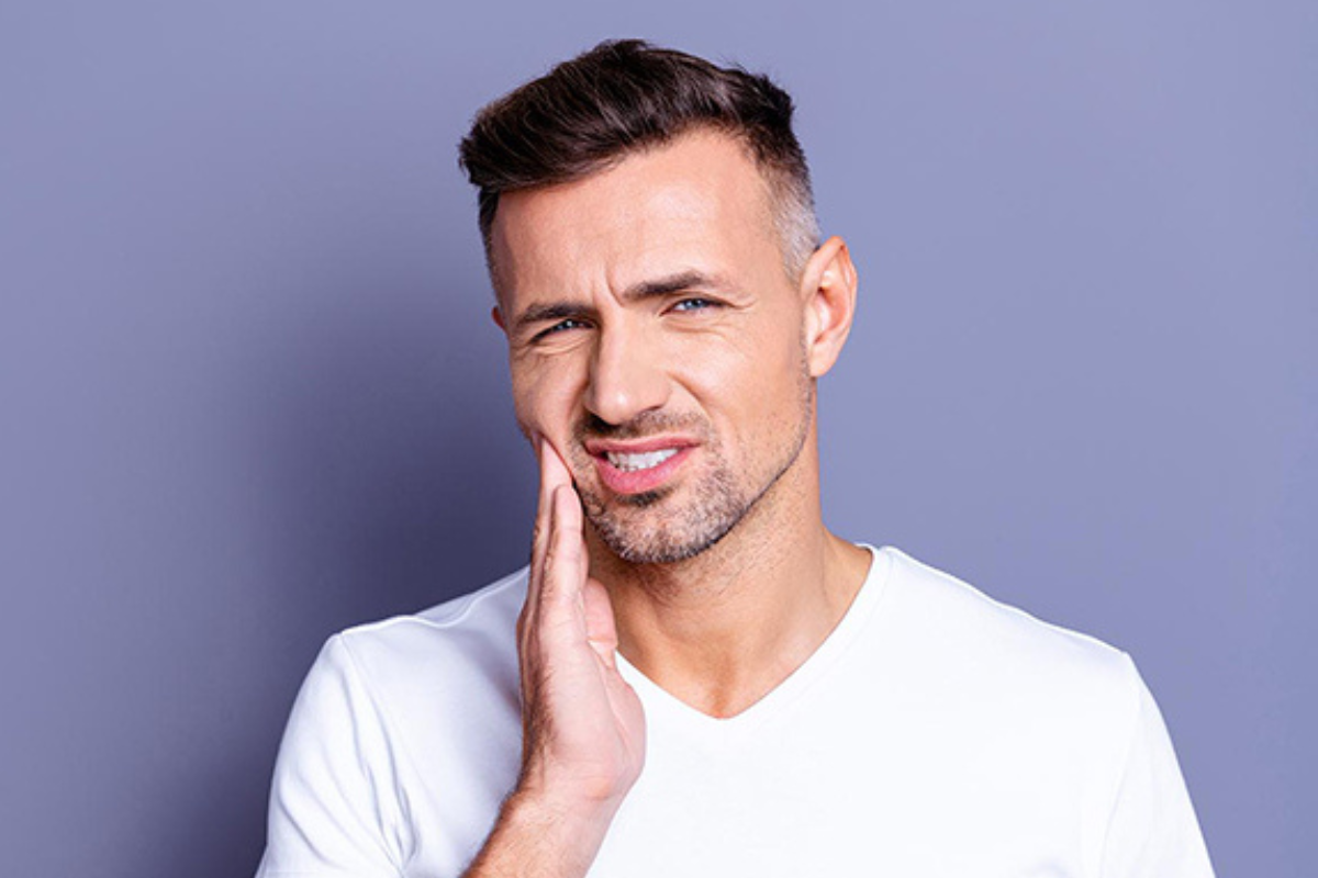 Man holding cheek in pain, experiencing dental abscess symptoms requiring emergency dental care.