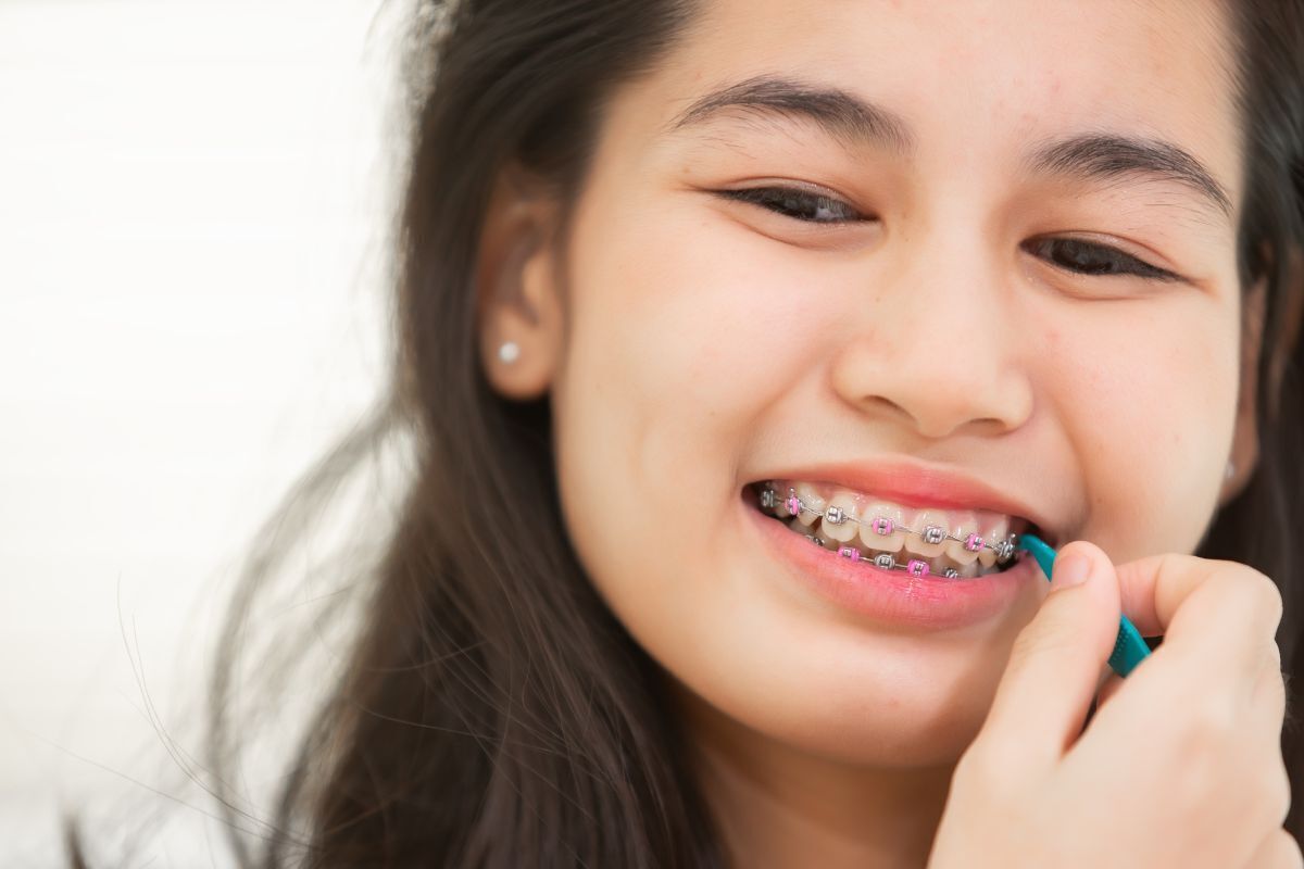 Young patient displaying metal braces with pink bands during cosmetic dental treatment in Brooklyn.