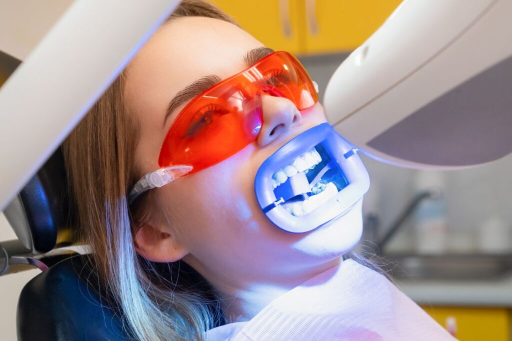 Patient receiving GLO Science teeth whitening treatment with blue LED light technology in Brooklyn dental office.