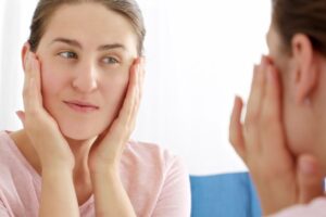 Woman examining her face in mirror during cosmetic consultation appointment.