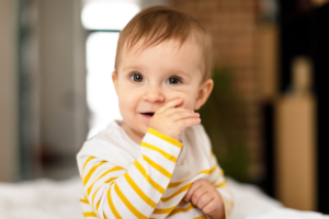 Happy toddler in yellow and white striped shirt with hand near mouth, illustrating thumb sucking habit.