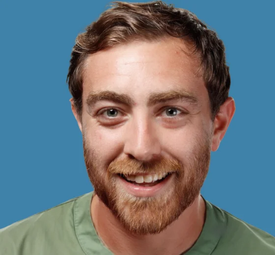 Professional headshot of a smiling male dental professional with red hair and beard