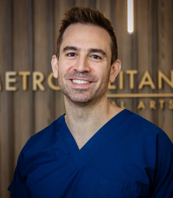 Professional headshot of a smiling male dentist wearing blue medical attire