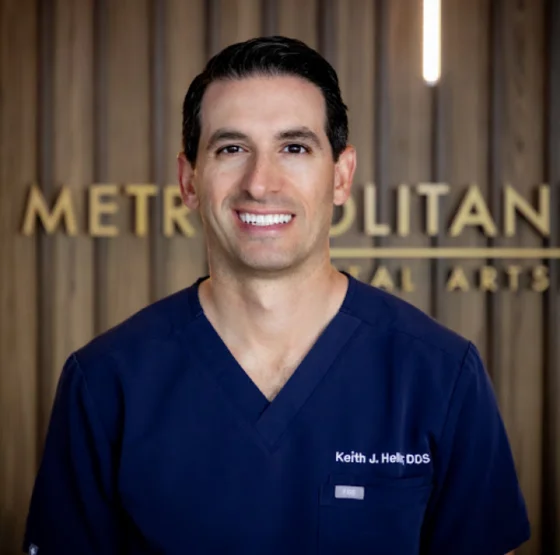 Professional headshot of a smiling male dentist wearing blue medical attire