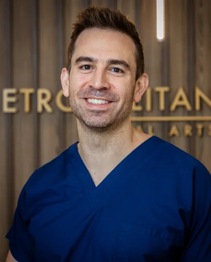 Professional headshot of a man wearing blue medical scrubs