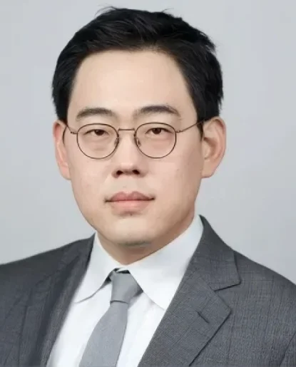 Professional headshot of a man wearing a light-colored shirt and glasses