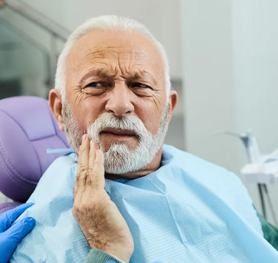 Older man touching his cheek while looking at the camera