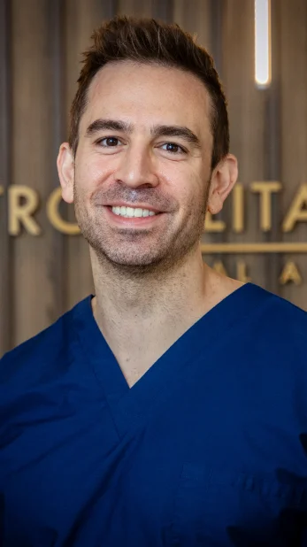 Professional headshot of a man wearing blue medical scrubs