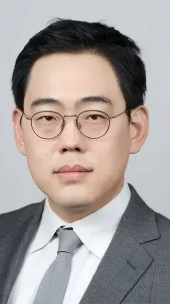 Professional headshot of a man wearing a light-colored shirt and glasses