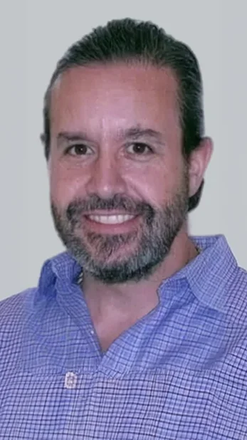 Professional headshot of a man with a beard wearing a light blue shirt