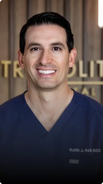Professional headshot of a smiling male dentist wearing blue medical attire