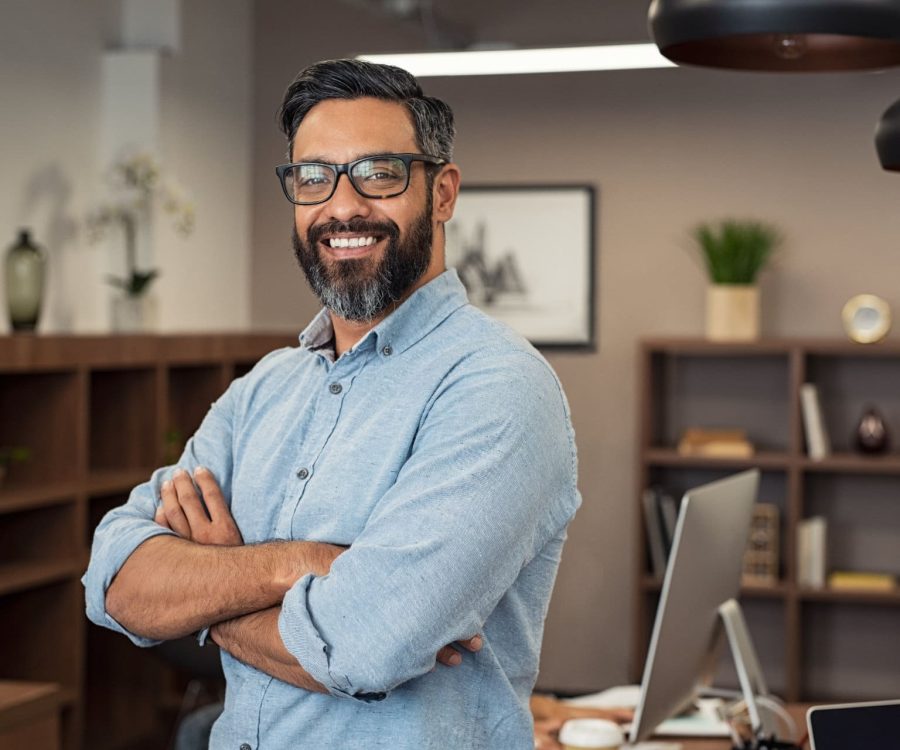 Portrait of happy mature businessman wearing spectacles and looking at camera. Multiethnic satisfied man with beard and eyeglasses feeling confident at office. Successful middle eastern business man smiling in a creative office.