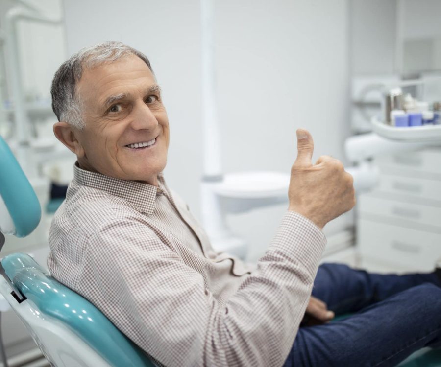 Old senior man sitting in a dental chair thumb up