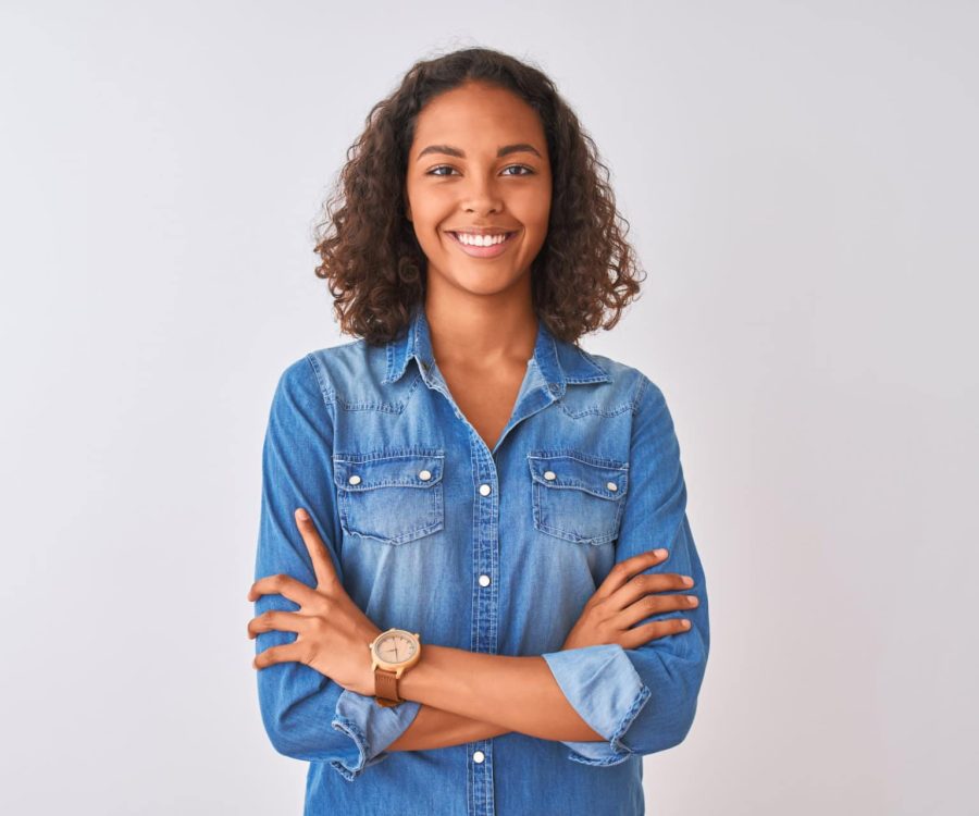 Young brazilian woman wearing denim shirt standing over isolated white background happy face smiling with crossed arms looking at the camera. Positive person.
